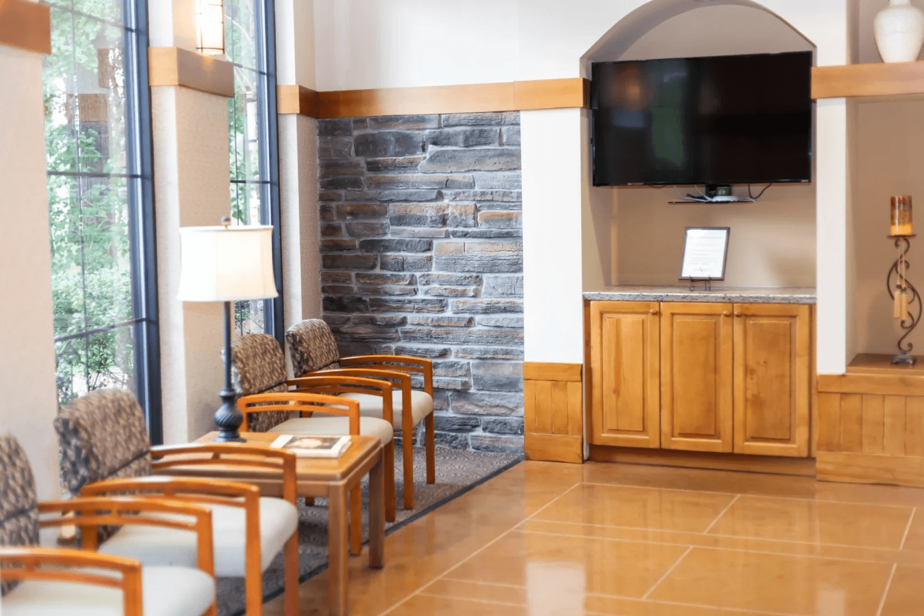 The Oak Hills Dentistry waiting room with armchairs, a stone feature wall and tall windows