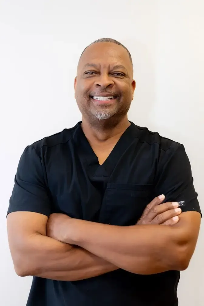 Gerald, registered dental assistant at Oak Hills Dentistry, smiling with his arms folded in black scrubs