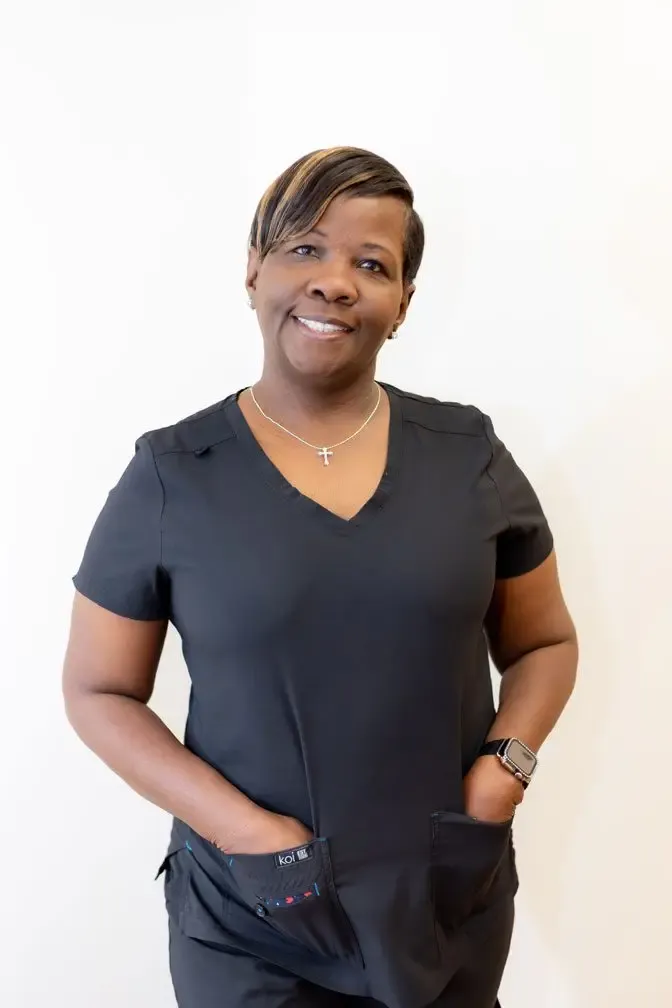 Pat, operations manager at Oak Hills Dentistry, smiling in black scrubs against a white wall
