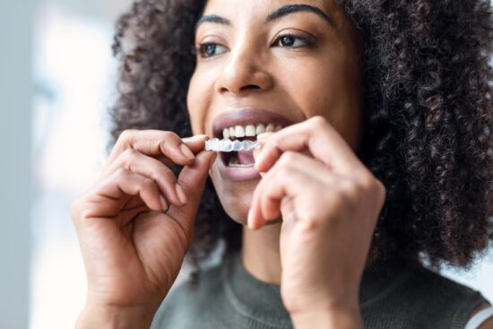 closeup of a young woman putting in her Invisalign, clear aligner therapy