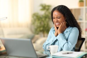 young professional sitting at her desk struggling with jaw pain, possible TMJ
