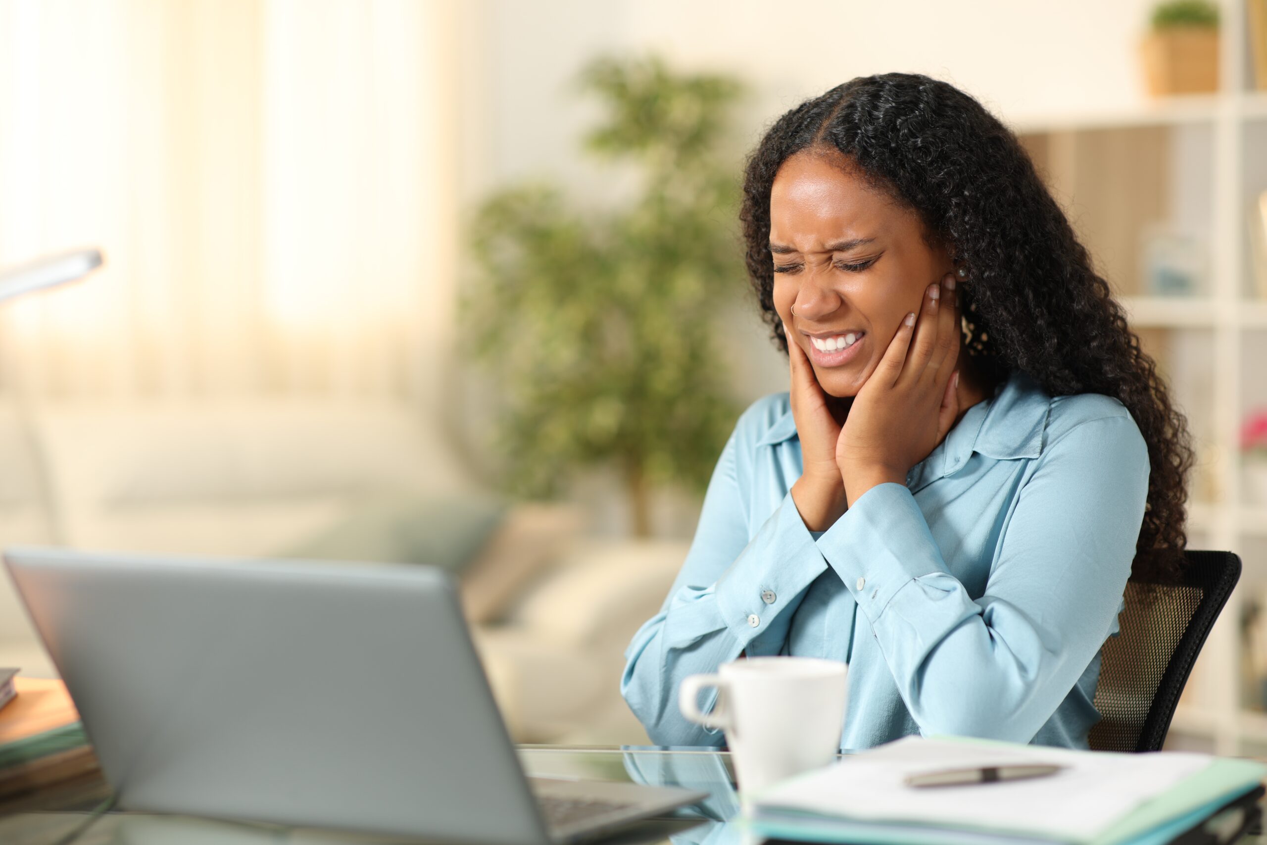 young professional sitting at her desk struggling with jaw pain, possible TMJ