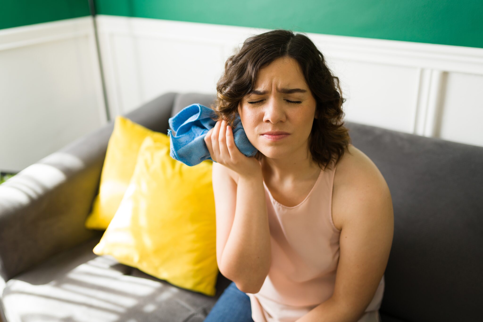 young woman on couch with ice pack on jaw, severe tooth pain