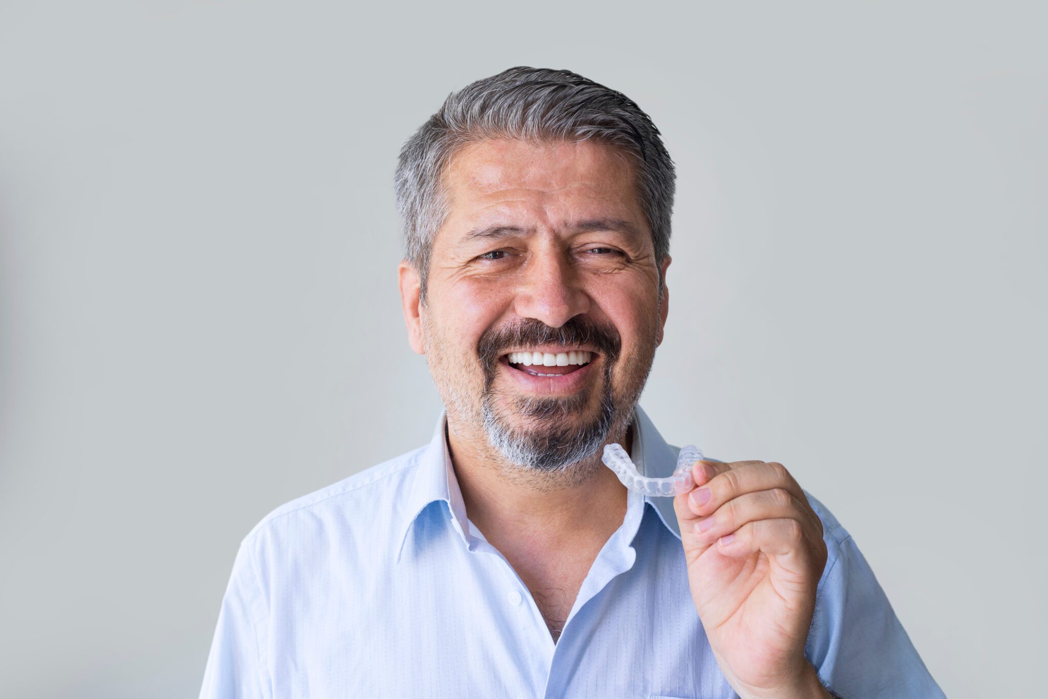 older man putting in his Invisalign against a grey background