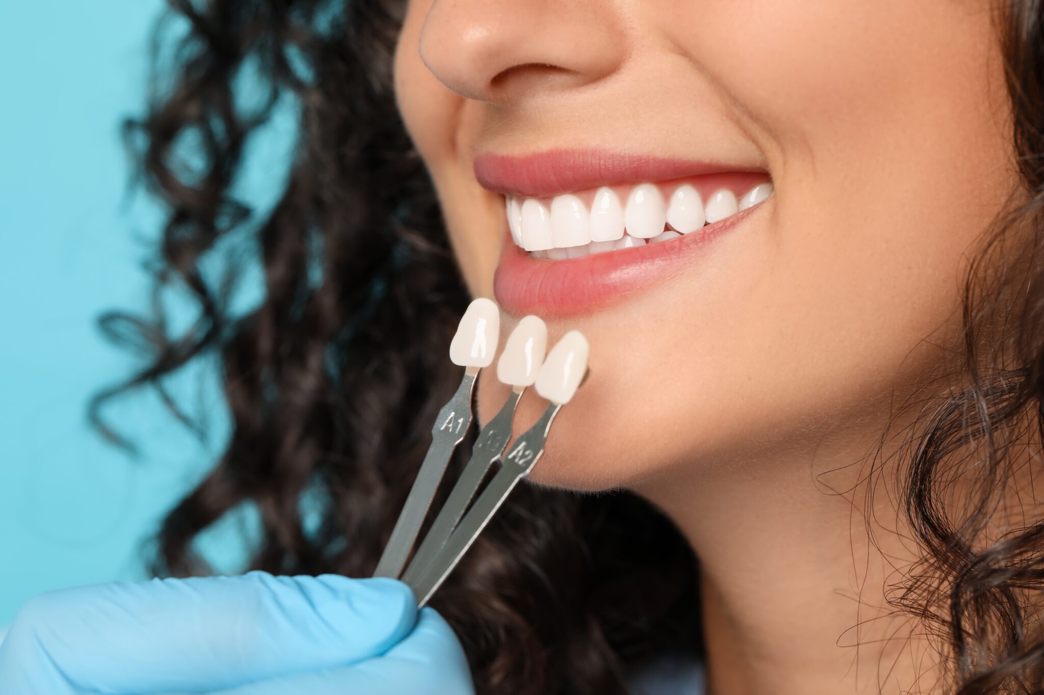 closeup of dentist holding veneer colors to a woman's teeth, light blue background