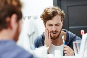 young man brushing his teeth in mirror, sensitive tooth pain